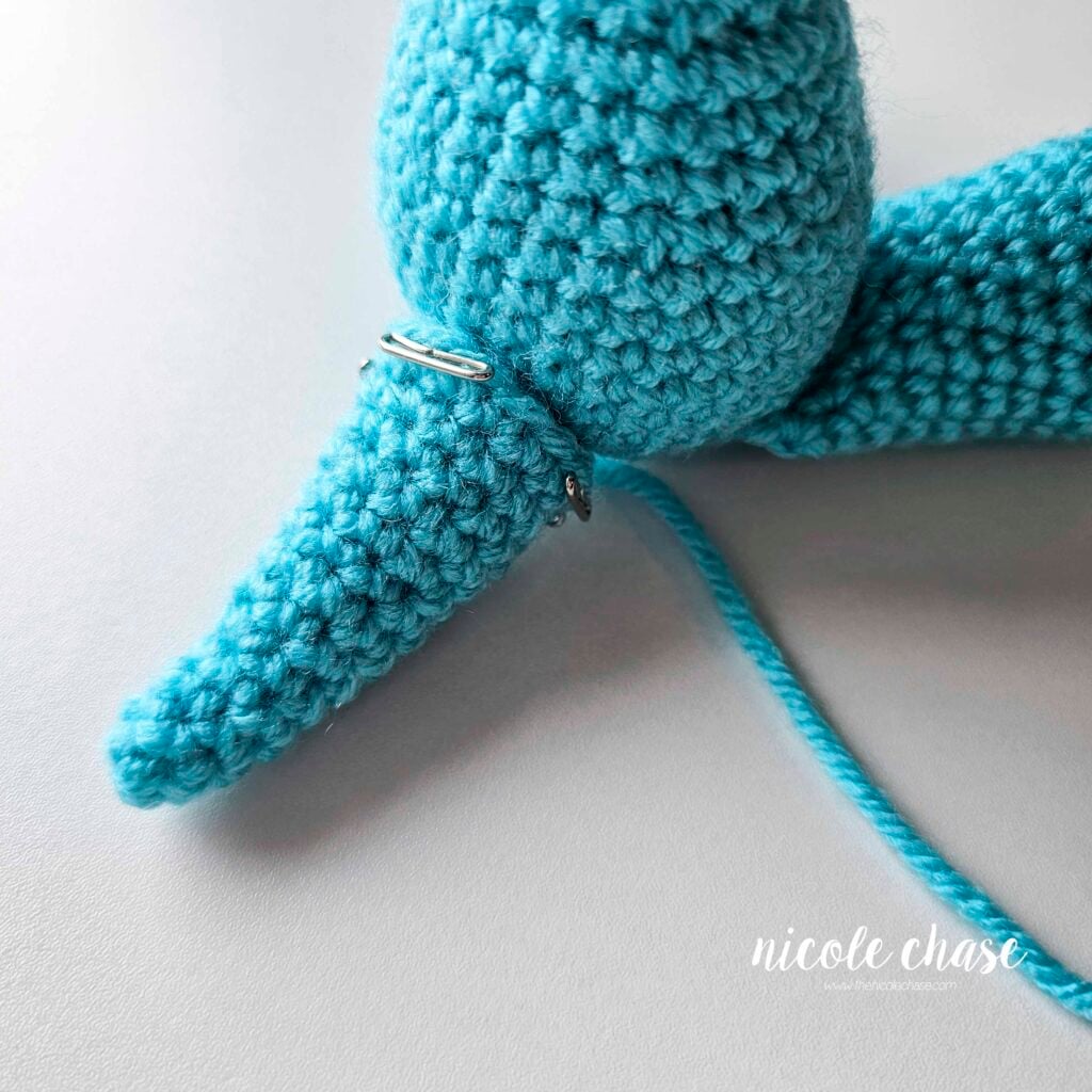 The tail has been pinned into place on the back of the crochet dragon's body and is awaiting sewing.