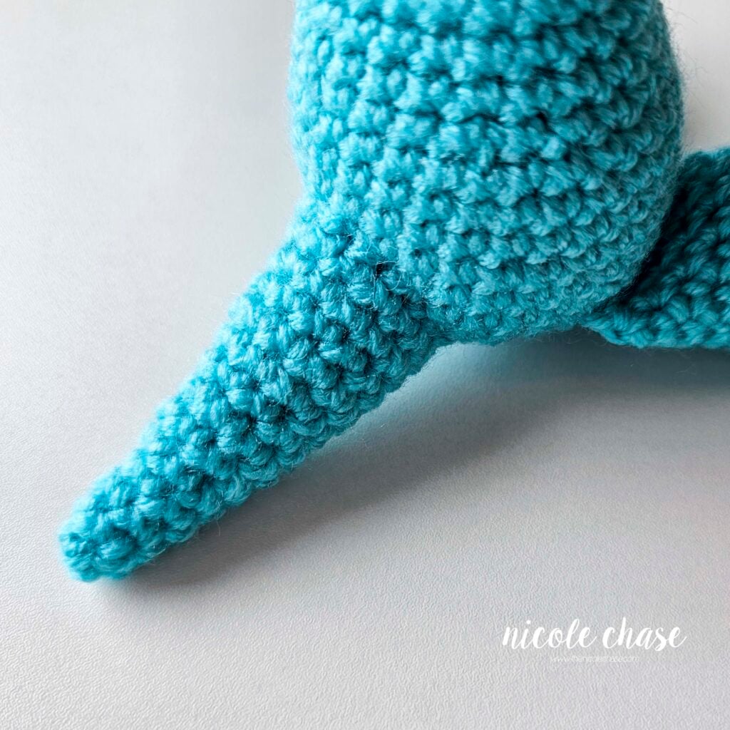 The crochet dragon tail sewn into place, with the dragon in a sitting position and a view of the tail from the side.