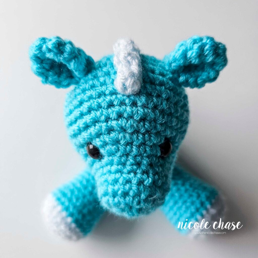 The ears of the crochet dragon have been sewn into place on each side of the top of the head, top down view from the front.