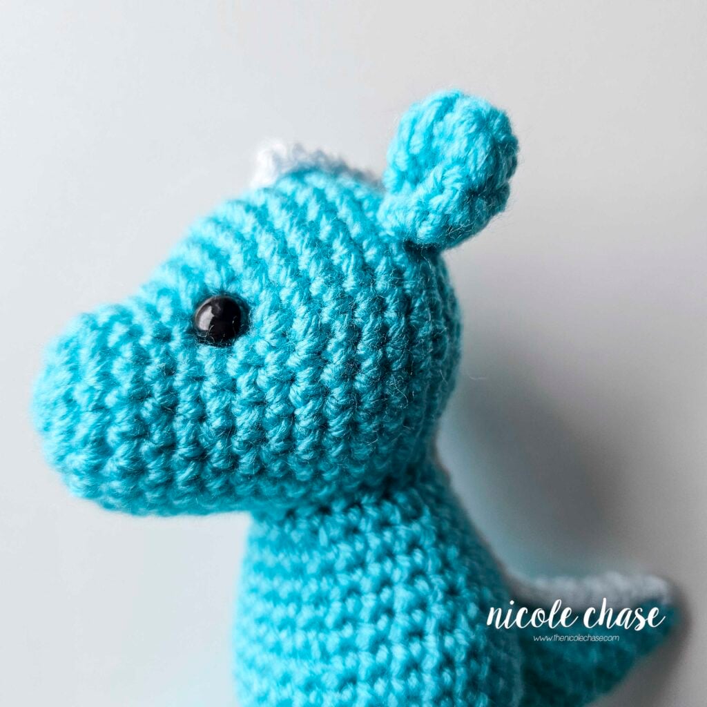 The ears of the crochet dragon have been sewn into place on each side of the top of the head, side profile view.