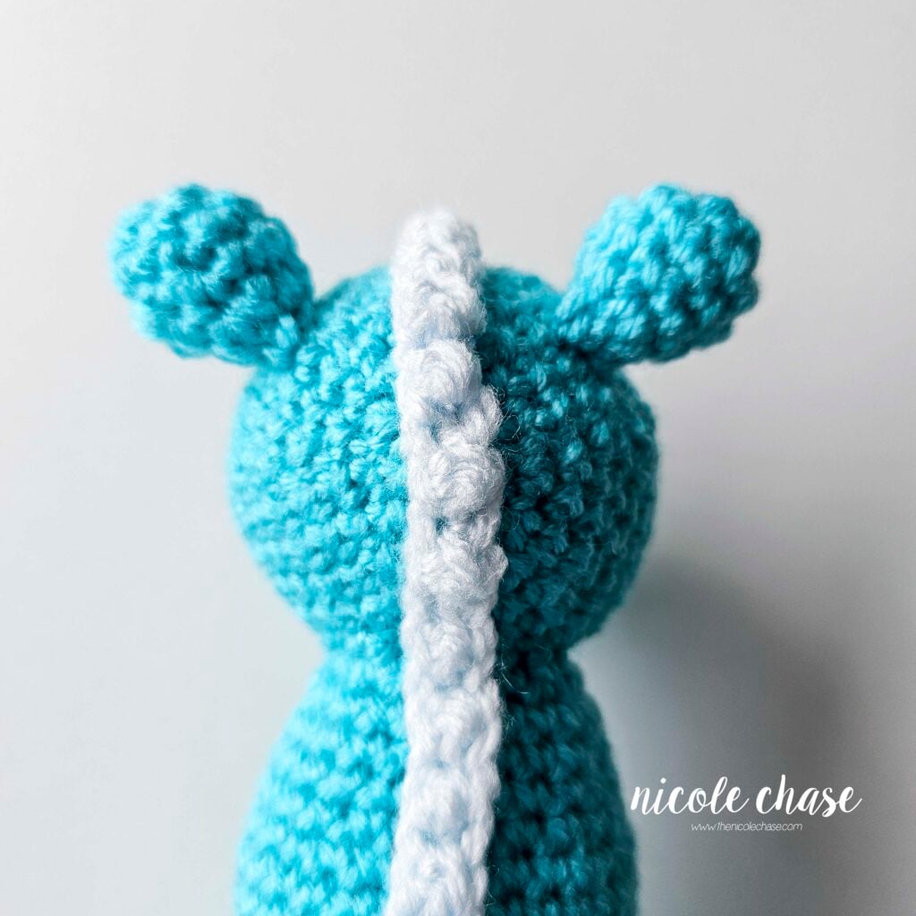 The ears of the crochet dragon have been sewn into place on each side of the top of the head, view from the back of the head.