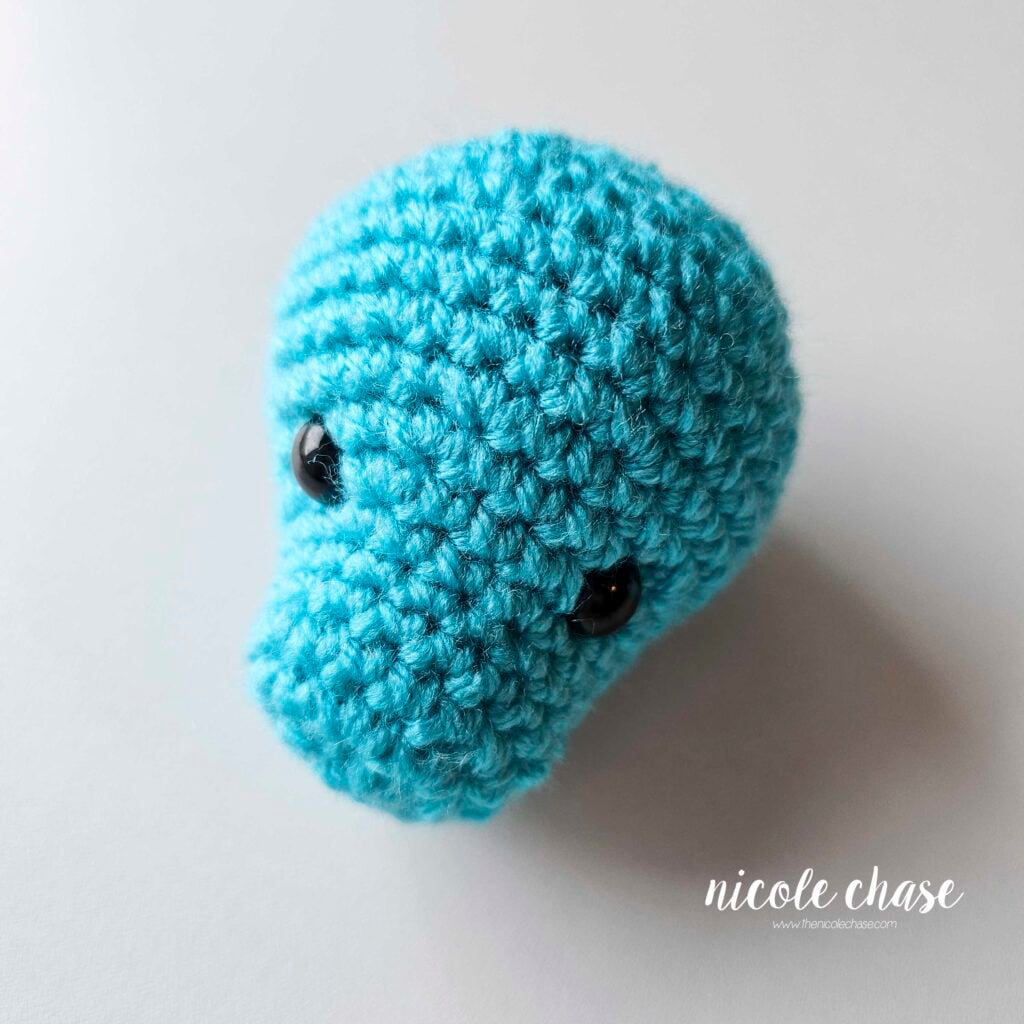 The finished crochet head of the dragon crochet pattern shown in bright blue yarn with black safety eyes.