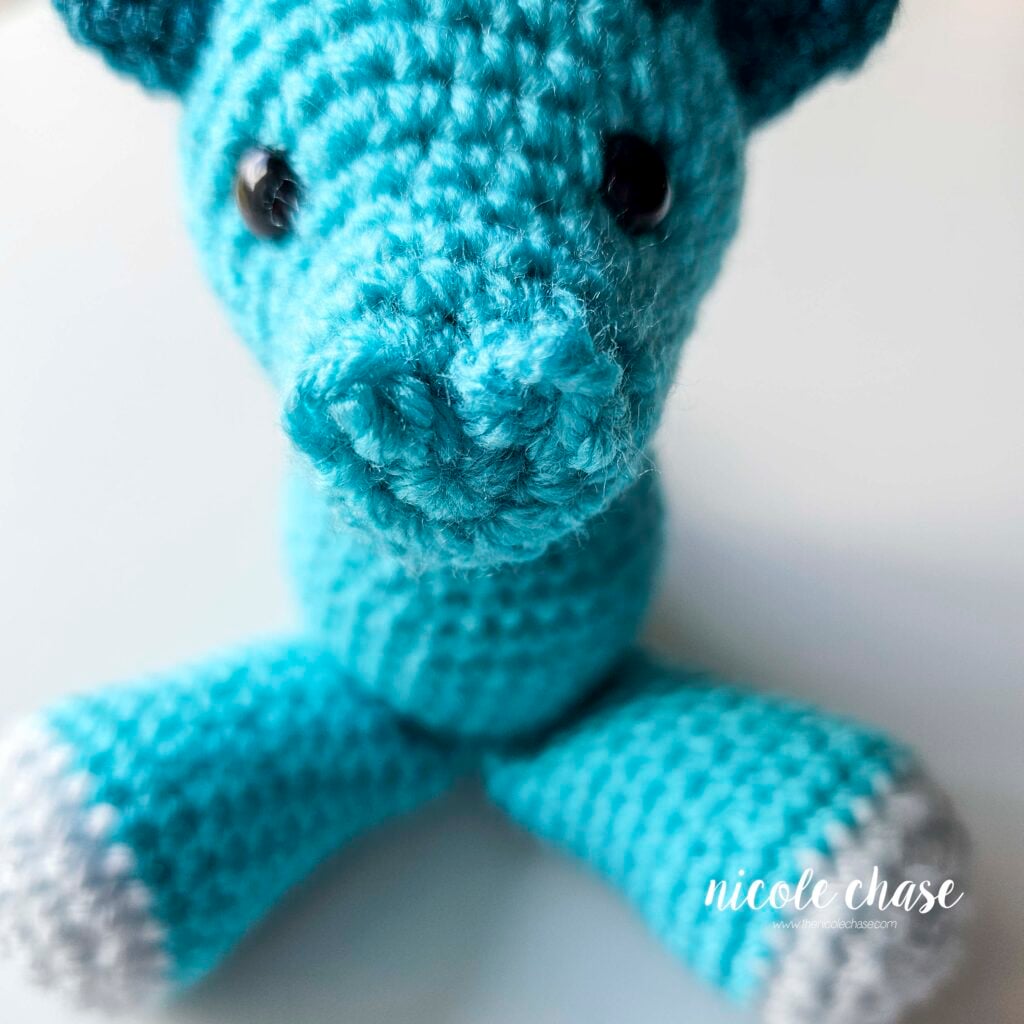 The crochet dragon's nostrils have been sewn into place on the front of the head, front view.