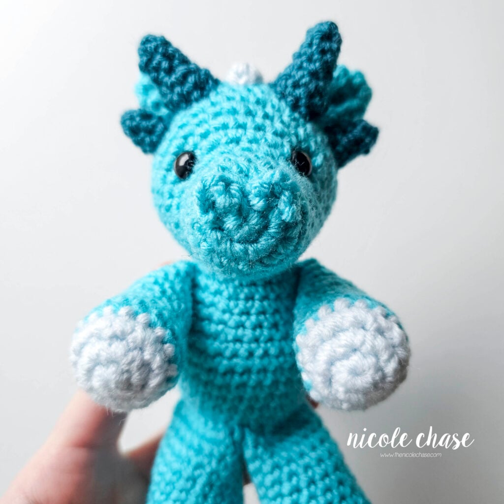 A front view of the crochet dragon with the arms sewn into place, and the arms are facing forward.