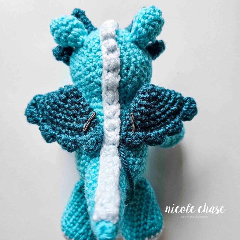 The dragon's crochet wings have been sewn into place on the back of the body, angled outward, and awaiting sewing.