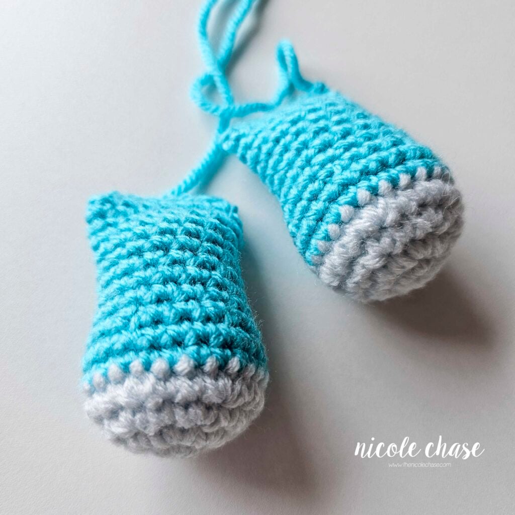 Two finished crochet legs made with light blue feet and bright blue colored legs. The legs are filled with stuffing, crocheted closed, and ready for assembly.