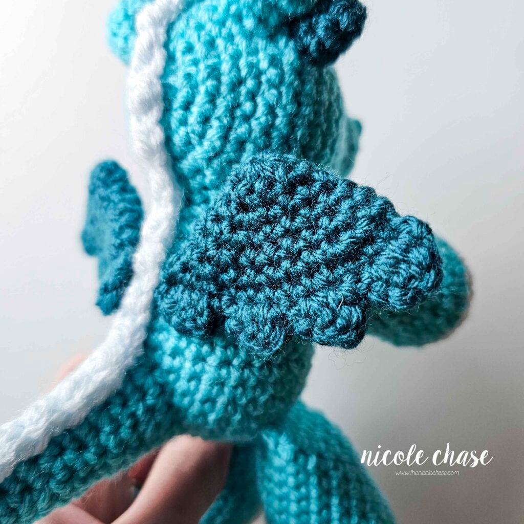 The teal dragon wings have been sewn into place on the back of the body. This is a close up view of the right side wing.