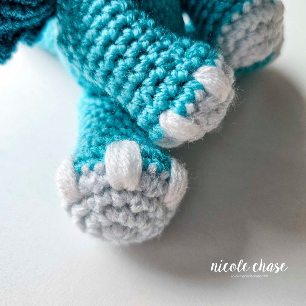 A close up view of embroidered nail details on the crochet dragon's arm and leg.