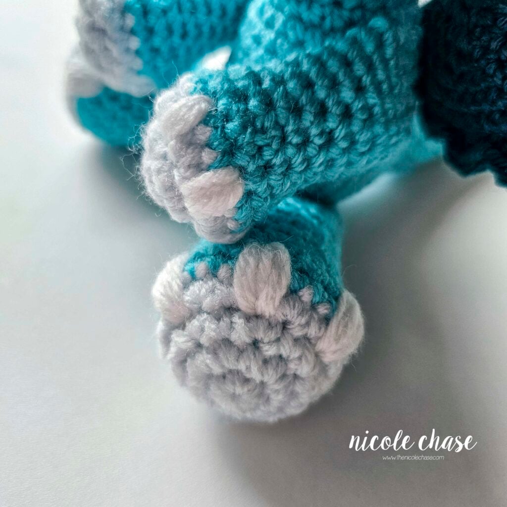 A close up view of embroidered nail details on the crochet dragon's other arm and leg.