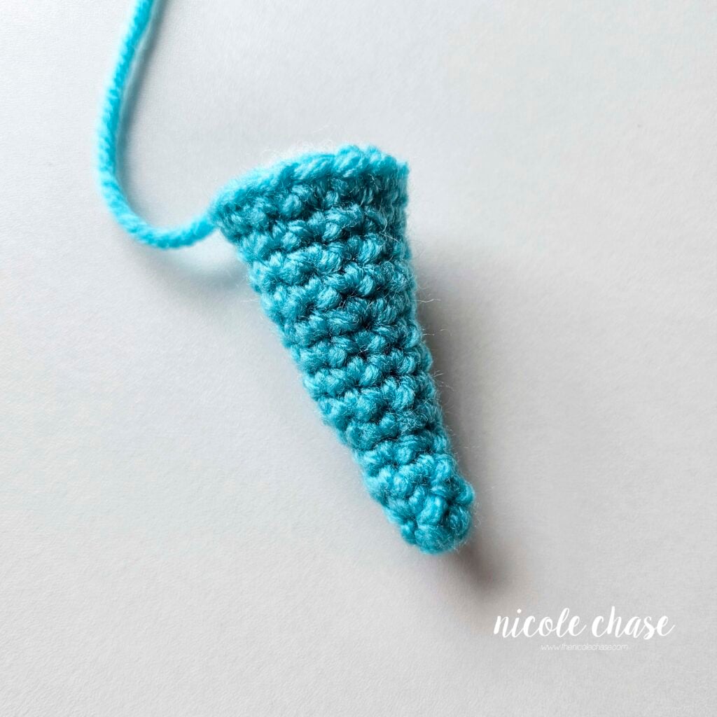 The finished tail of the amigurumi dragon made in bright blue yarn. The tail is filled with stuffing and ready for assembly.