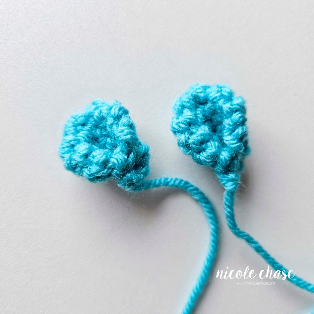 Two finished crochet ears with a pinched curve shape, made in bright blue yarn, ready for assembly.