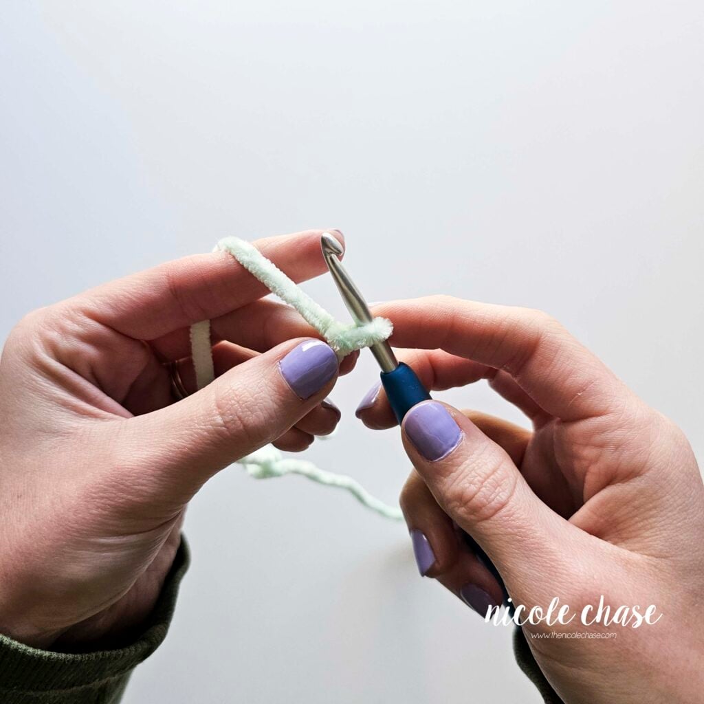Two hands crocheting with plush yarn, showing a slip knot on the hook. 