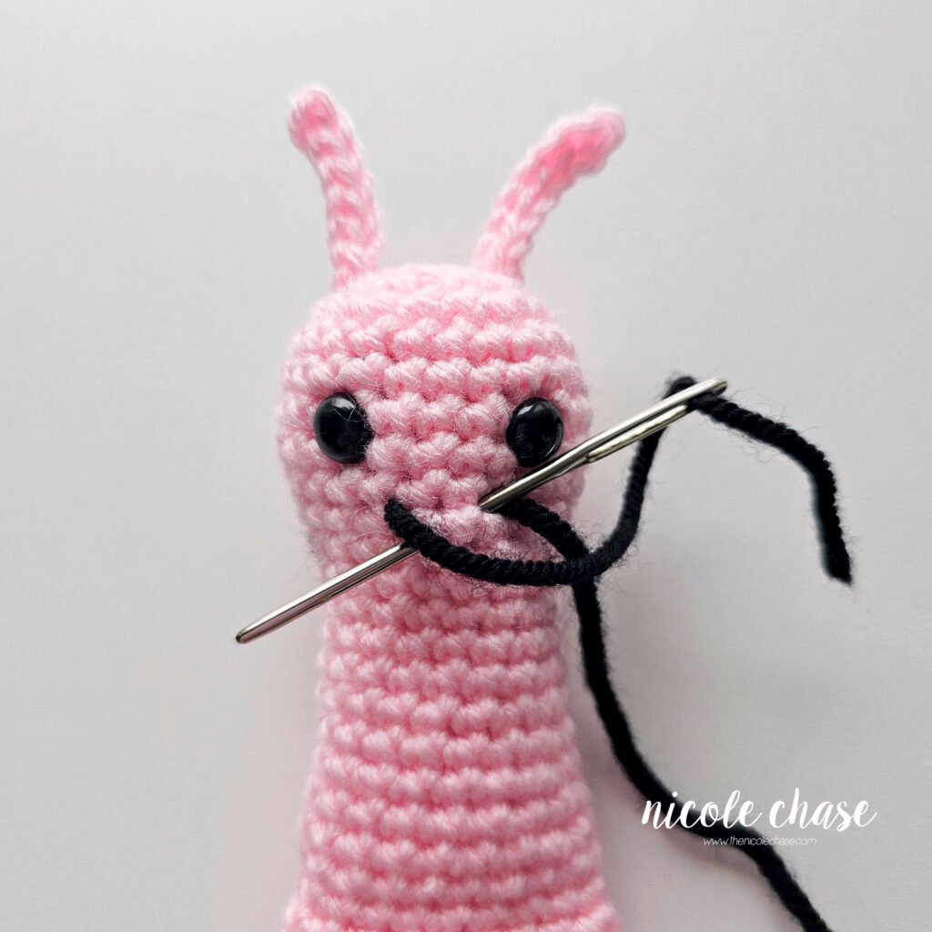 Embroidering a smile on the face of the crochet snail pattern with black yarn, step 2.