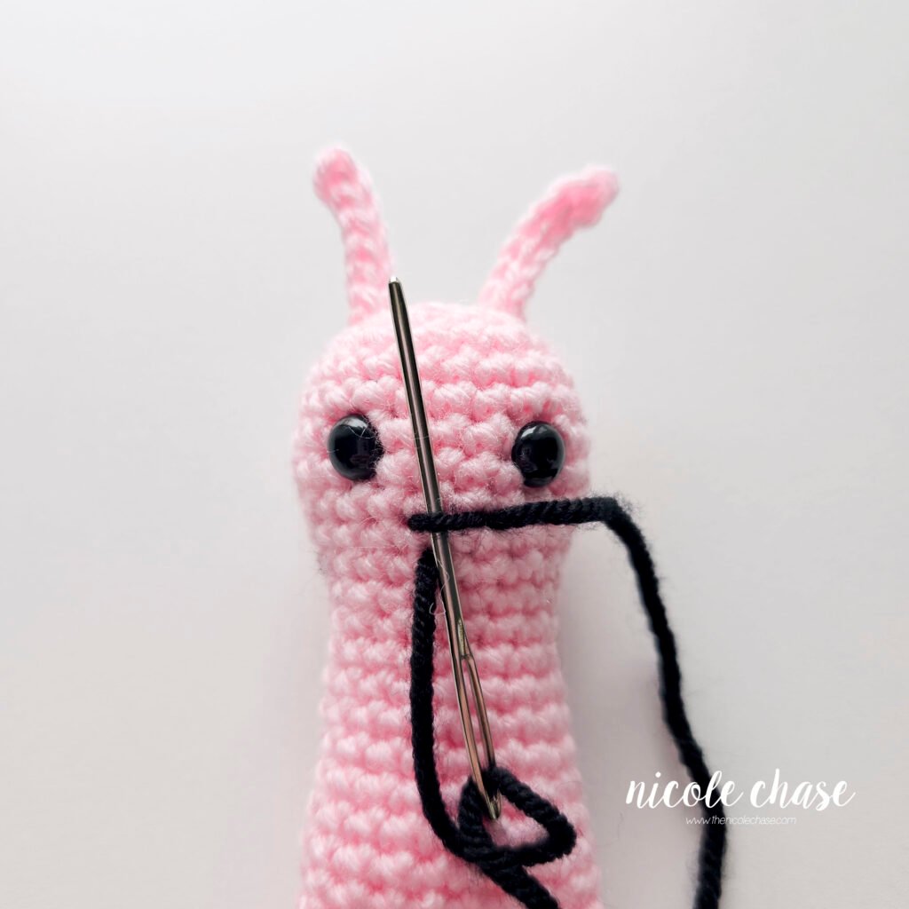 Embroidering a smile on the face of the crochet snail pattern with black yarn, step 3.