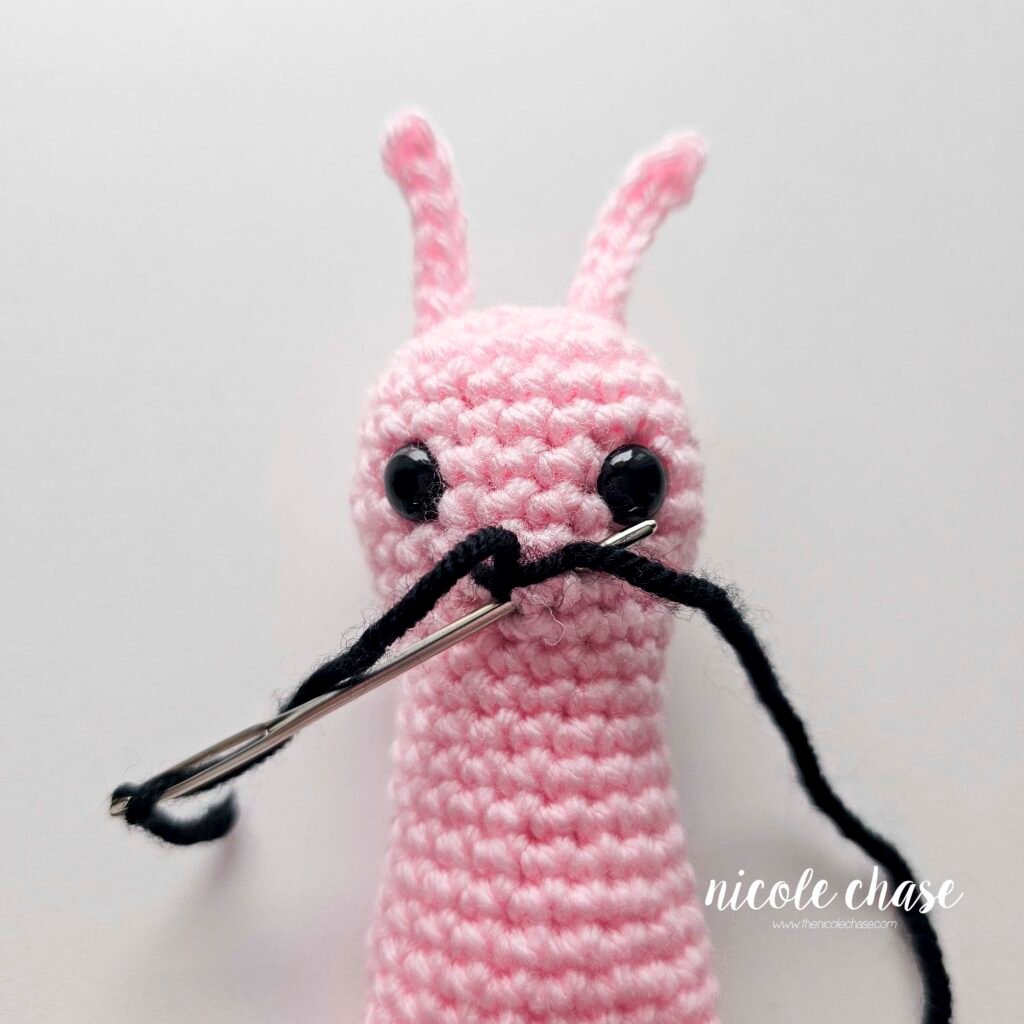 Embroidering a smile on the face of the crochet snail pattern with black yarn, step 4.