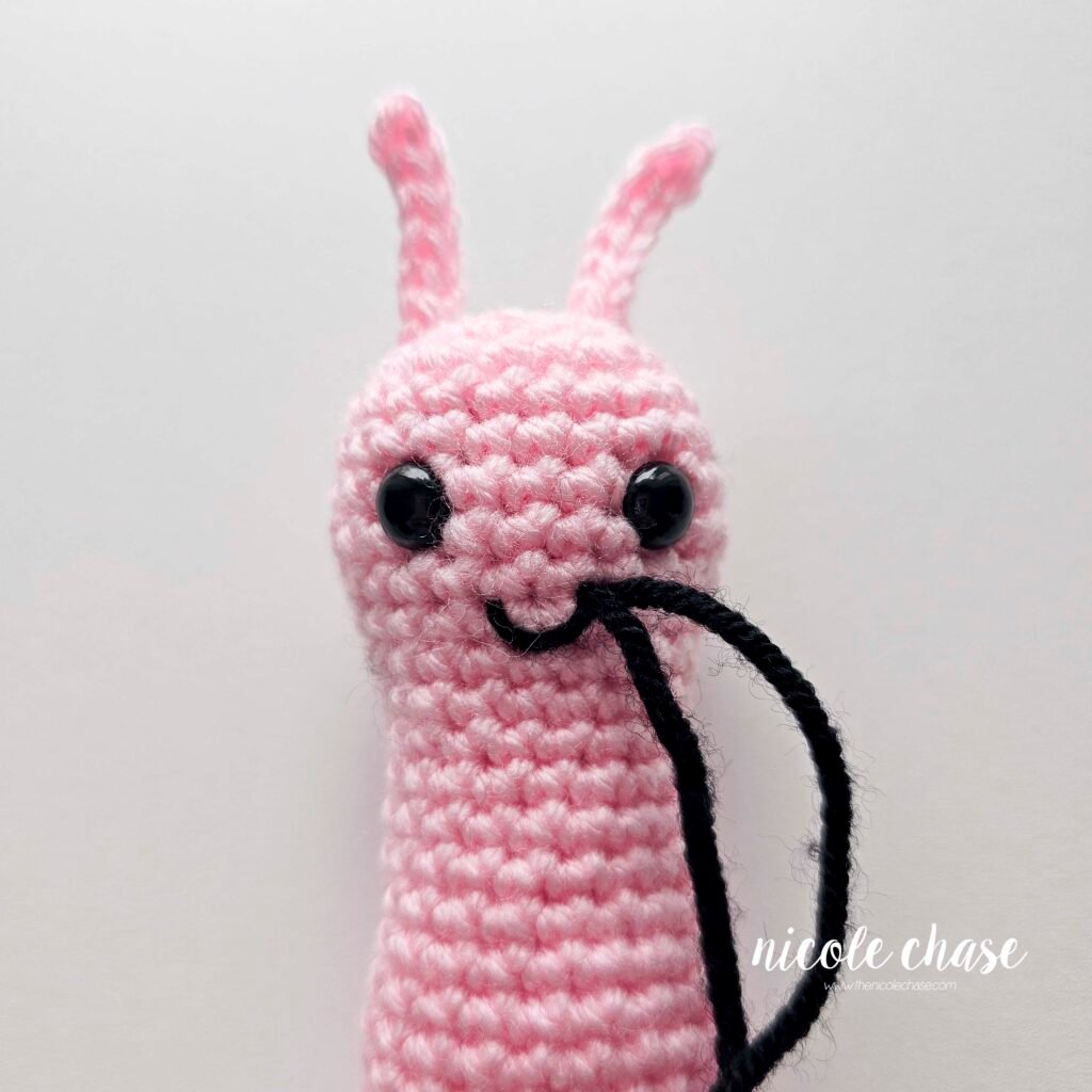 Embroidering a smile on the face of the crochet snail pattern with black yarn, step 5.