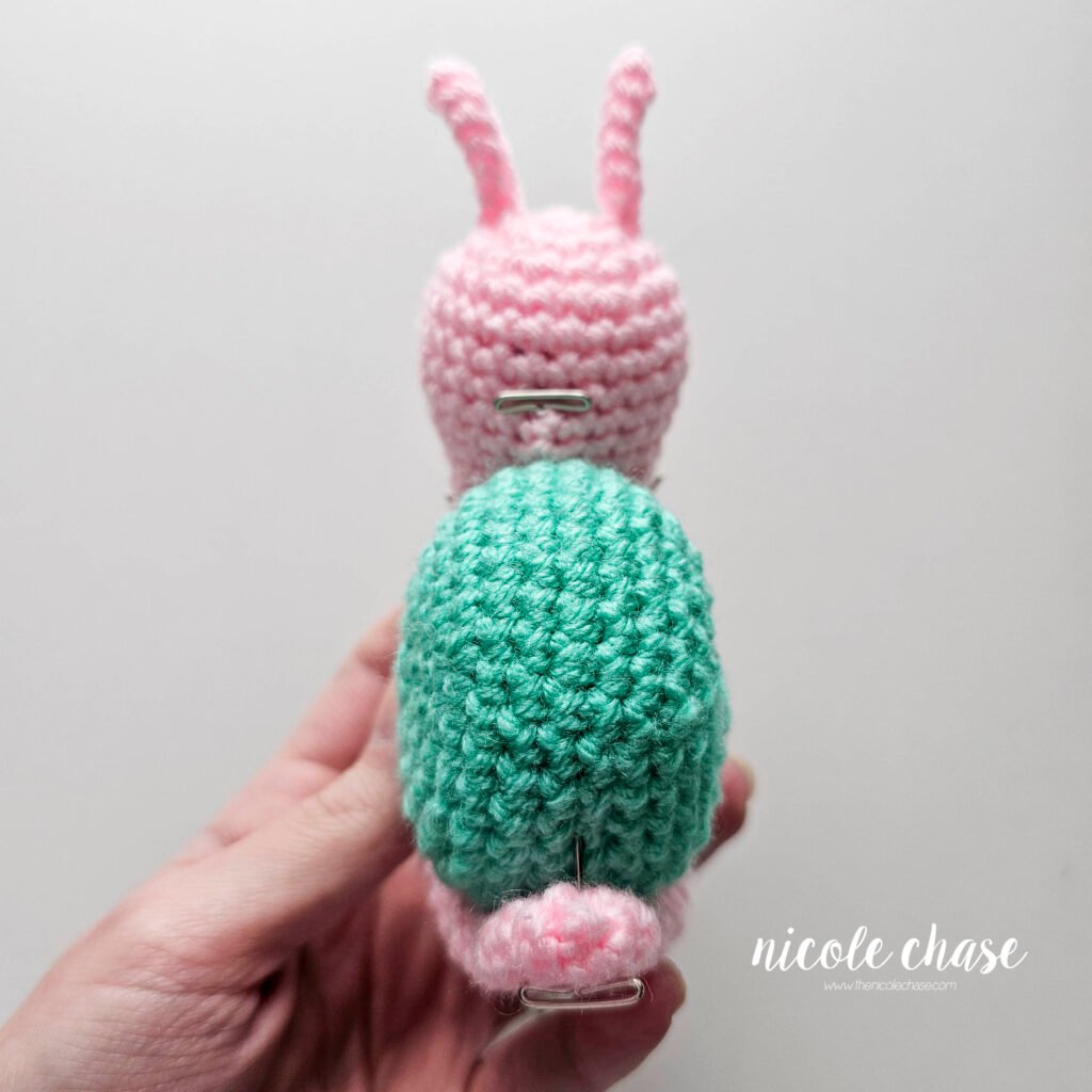Pinning the crochet snail's pink body in place curled around the teal shell prior to sewing, back view.