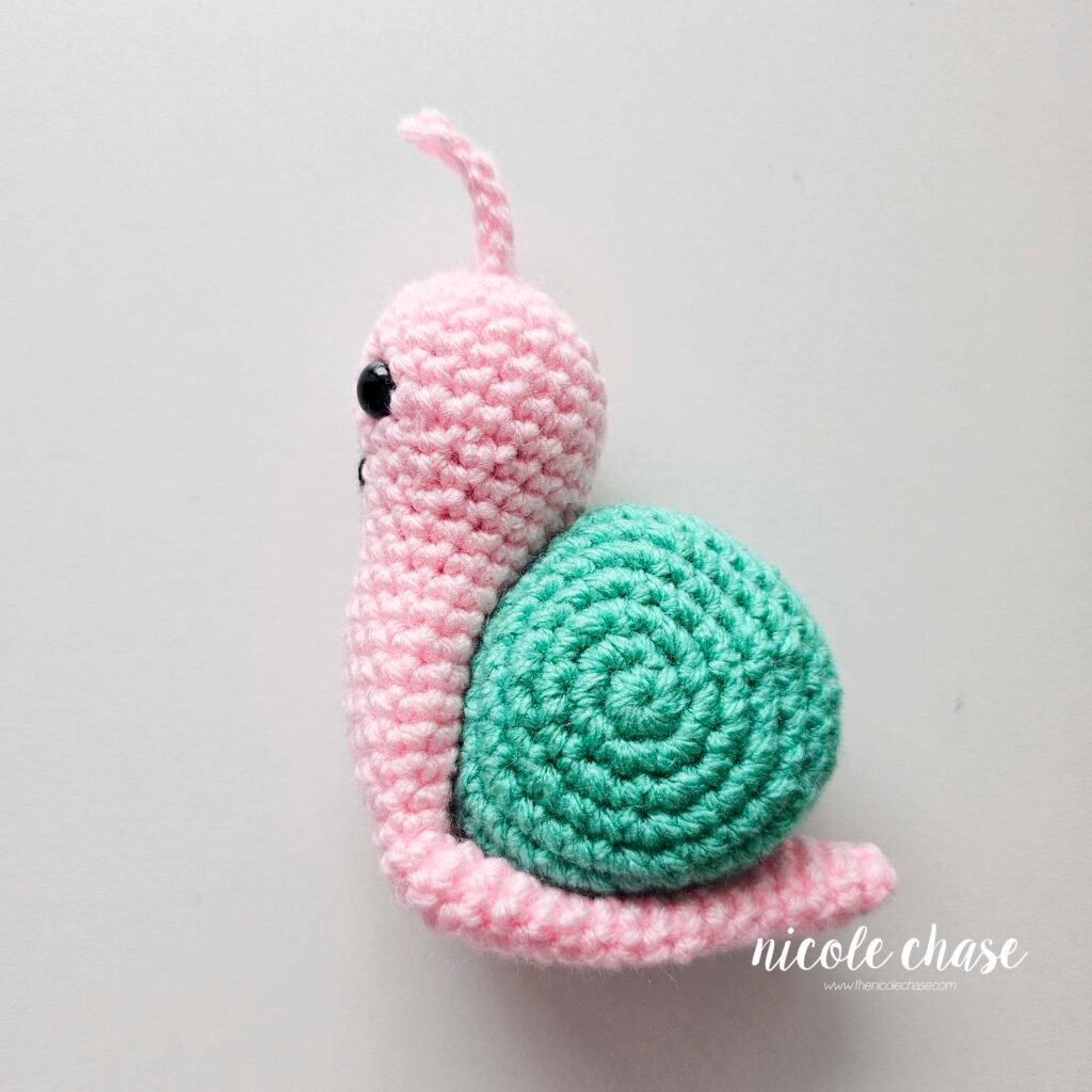 The body of the free snail crochet pattern has been pinned in place around the teal shell, view 1.