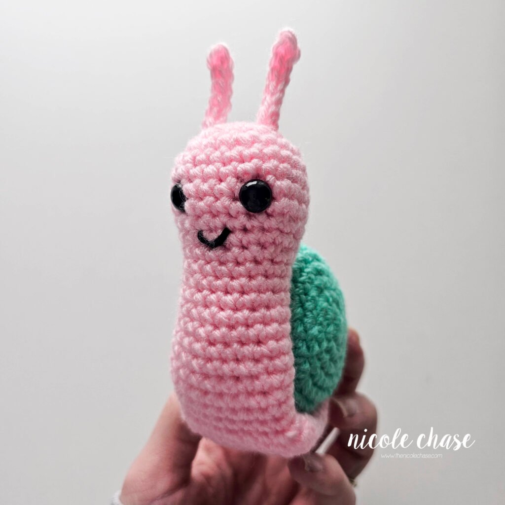 The body of the free snail crochet pattern has been pinned in place around the teal shell, view 3.