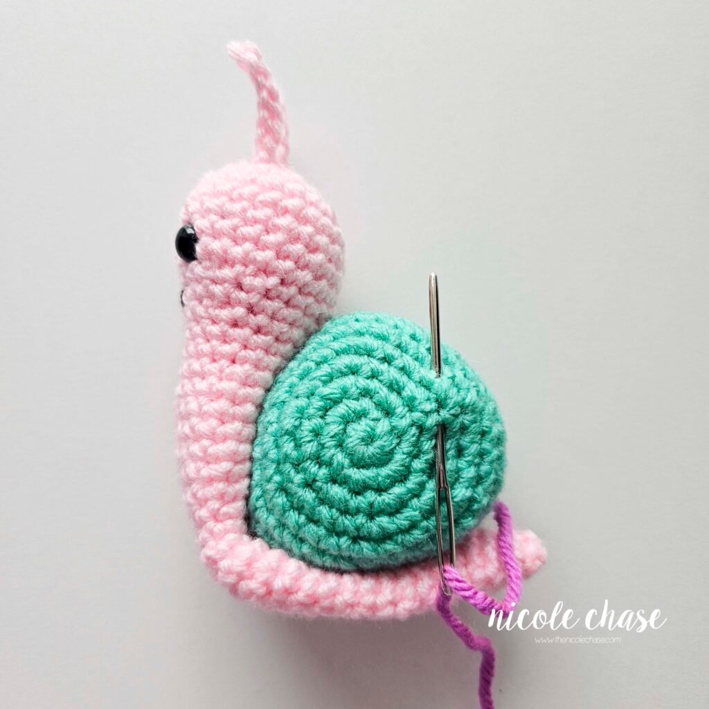 Embroidering a large flower on the shell of the crochet snail with purple yarn, step 1.