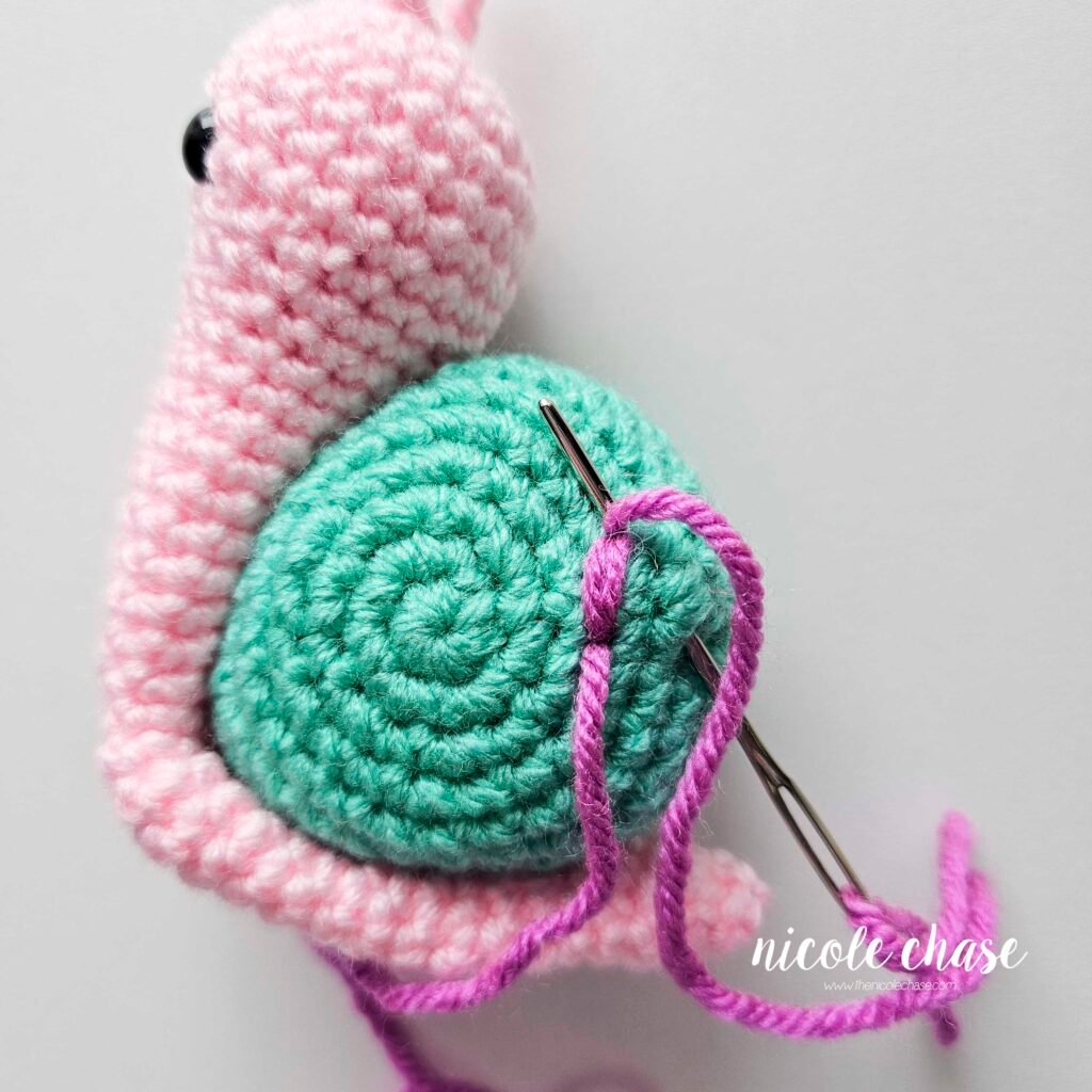 Embroidering a large flower on the shell of the crochet snail with purple yarn, step 2.