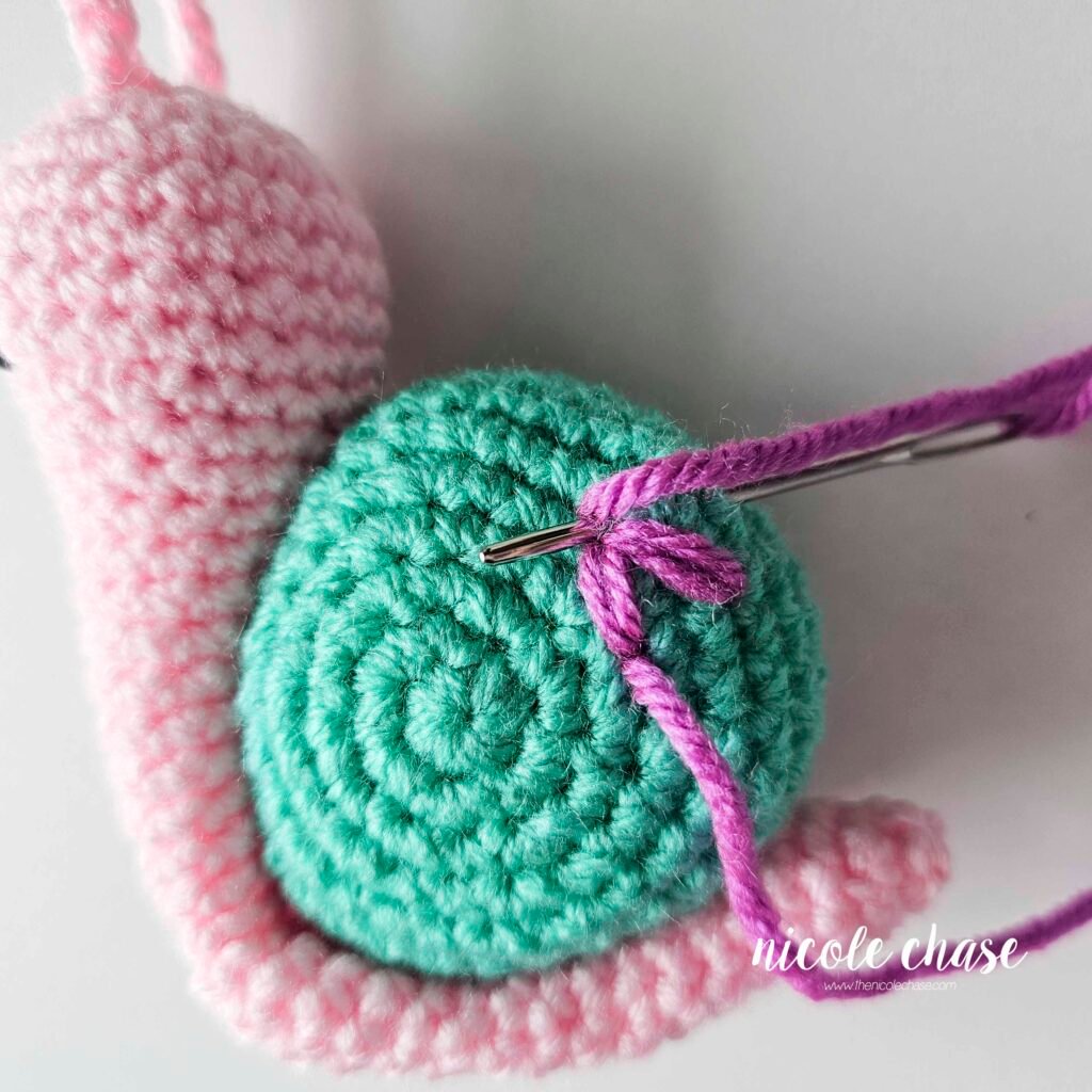 Embroidering a large flower on the shell of the crochet snail with purple yarn, step 3.