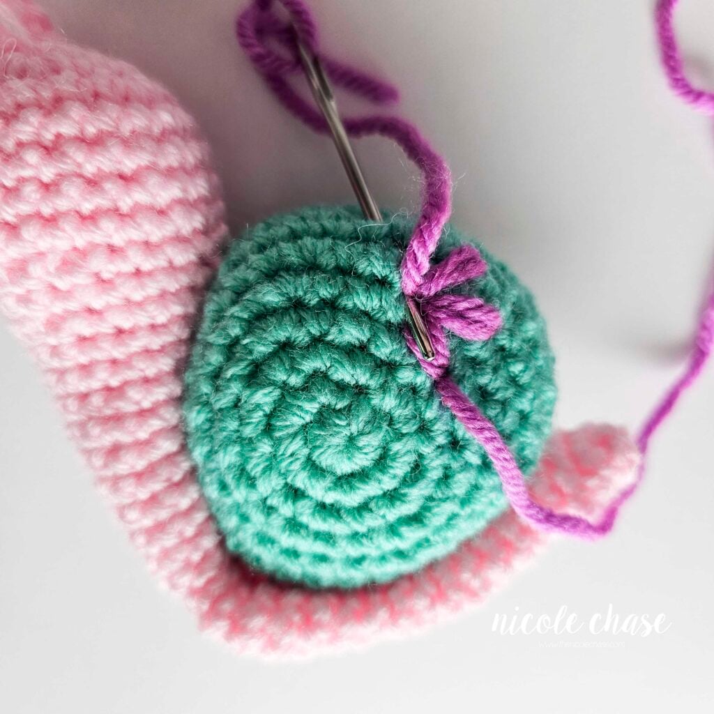 Embroidering a large flower on the shell of the crochet snail with purple yarn, step 4.