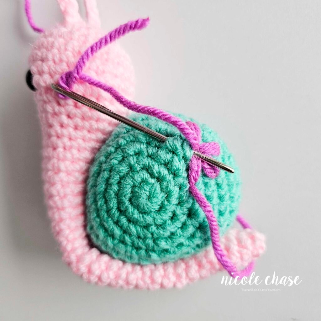 Embroidering a large flower on the shell of the crochet snail with purple yarn, step 5.
