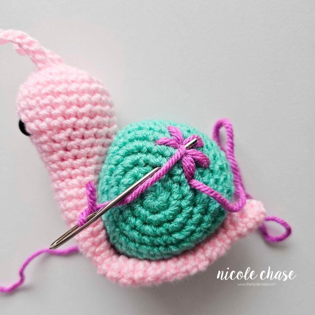Embroidering a large flower on the shell of the crochet snail with purple yarn, step 6.