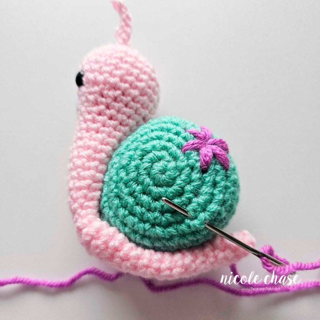 Embroidering a small flower on the shell of the crochet snail with purple yarn, step 1.