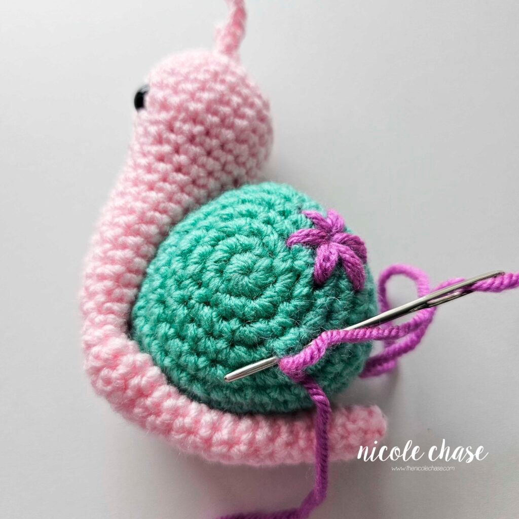 Embroidering a small flower on the shell of the crochet snail with purple yarn, step 2.