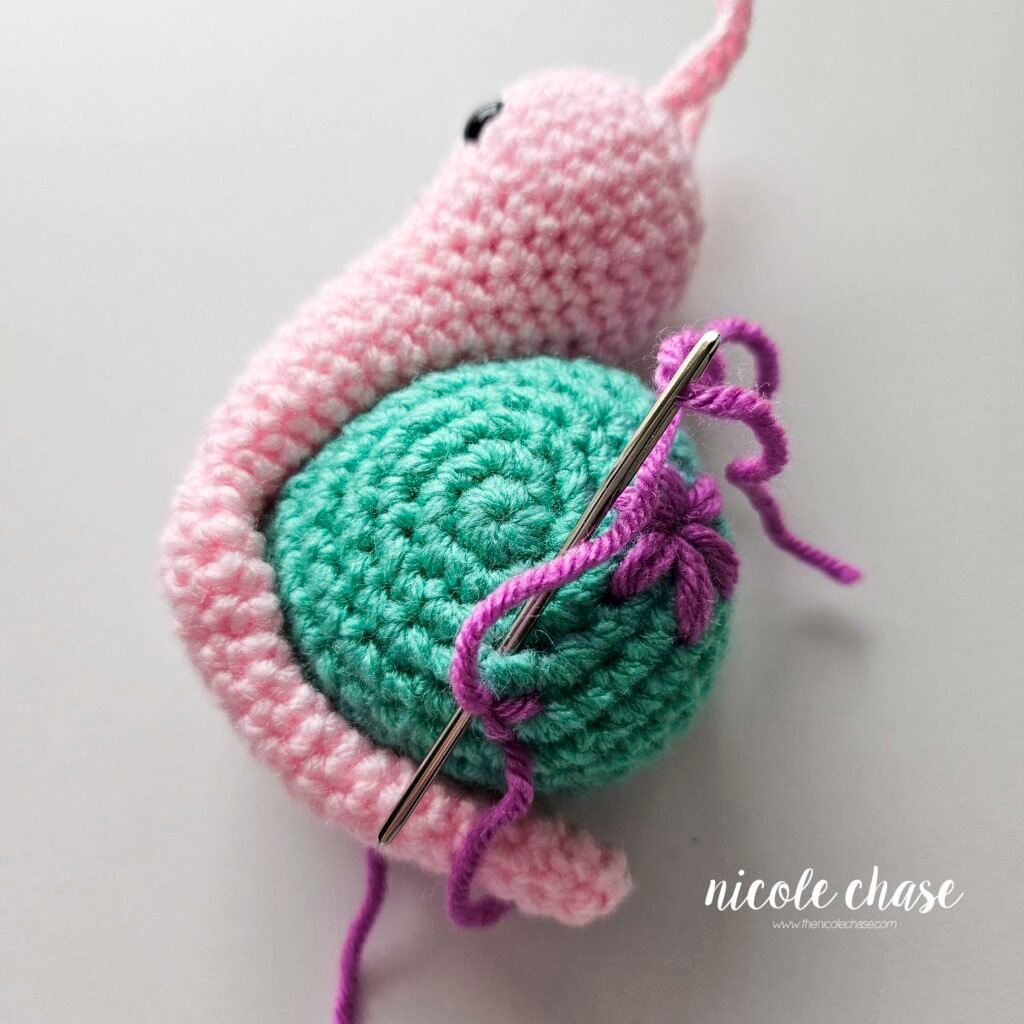 Embroidering a small flower on the shell of the crochet snail with purple yarn, step 3.
