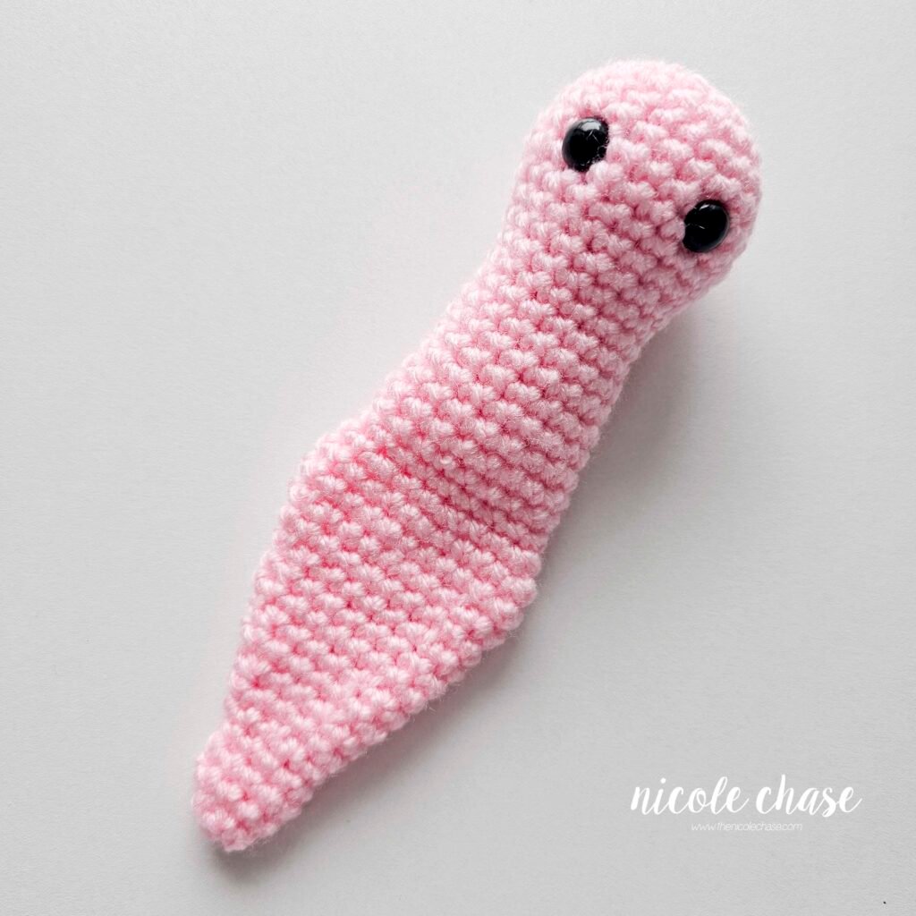 The finished body of the snail amigurumi pattern in pink yarn when it is laying flat.