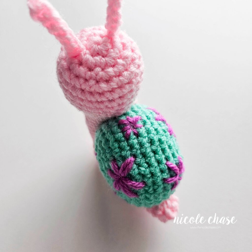 The shell of the free snail crochet pattern with a top down view showing the embroidered details of both a large flower and small flowers in purple yarn.