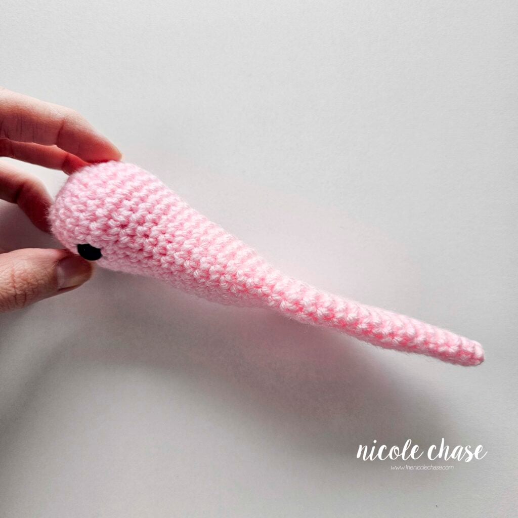 The finished body of the crochet snail in pink yarn shown from a side view to demonstrate the stuffing at the top of the head, but not in the lower part of the body.
