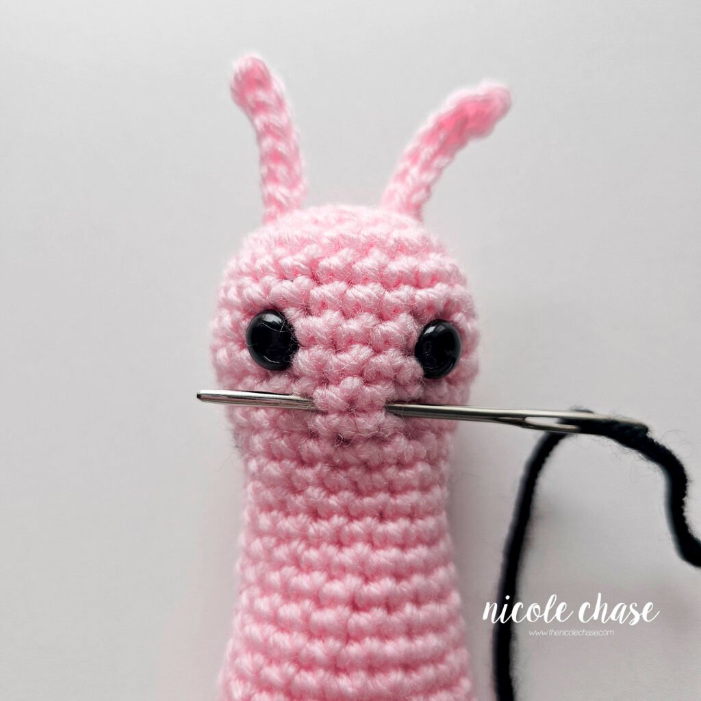 Embroidering a smile on the face of the crochet snail pattern with black yarn, step 1.