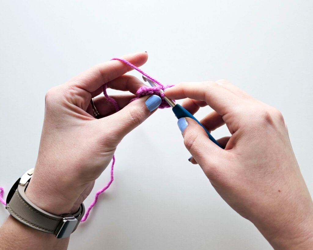 View of a person using the knife grip on a blue ergonomic crochet hook while maintaining yarn tension with their non-dominant hand.