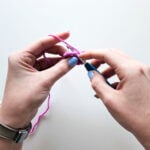 View of a person using the knife grip on a blue ergonomic crochet hook while maintaining yarn tension with their non-dominant hand.