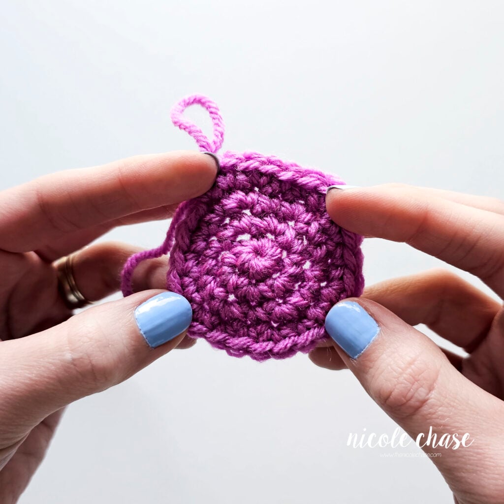 A close up of a round crochet swatch in purple yarn with loose single crochet stitches.