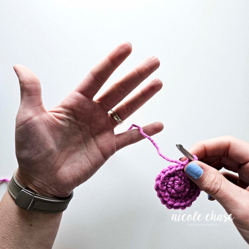 A close-up photo showing the yarn being threaded over the left pinky, between the pinky and ring finger. 