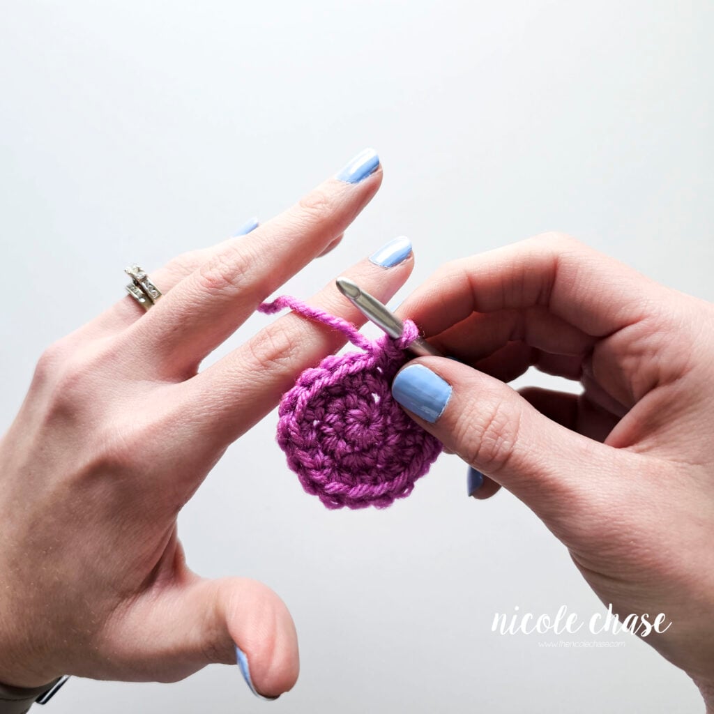 A close-up demonstrating the yarn then begin threaded between the middle and pointer finger, for controlling tension. 