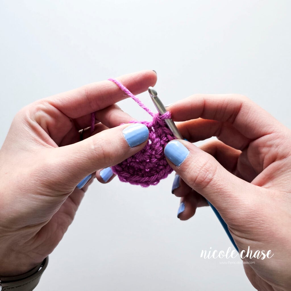 A close-up photo showing the thumb and middle fingers coming together to hold the crochet piece. 