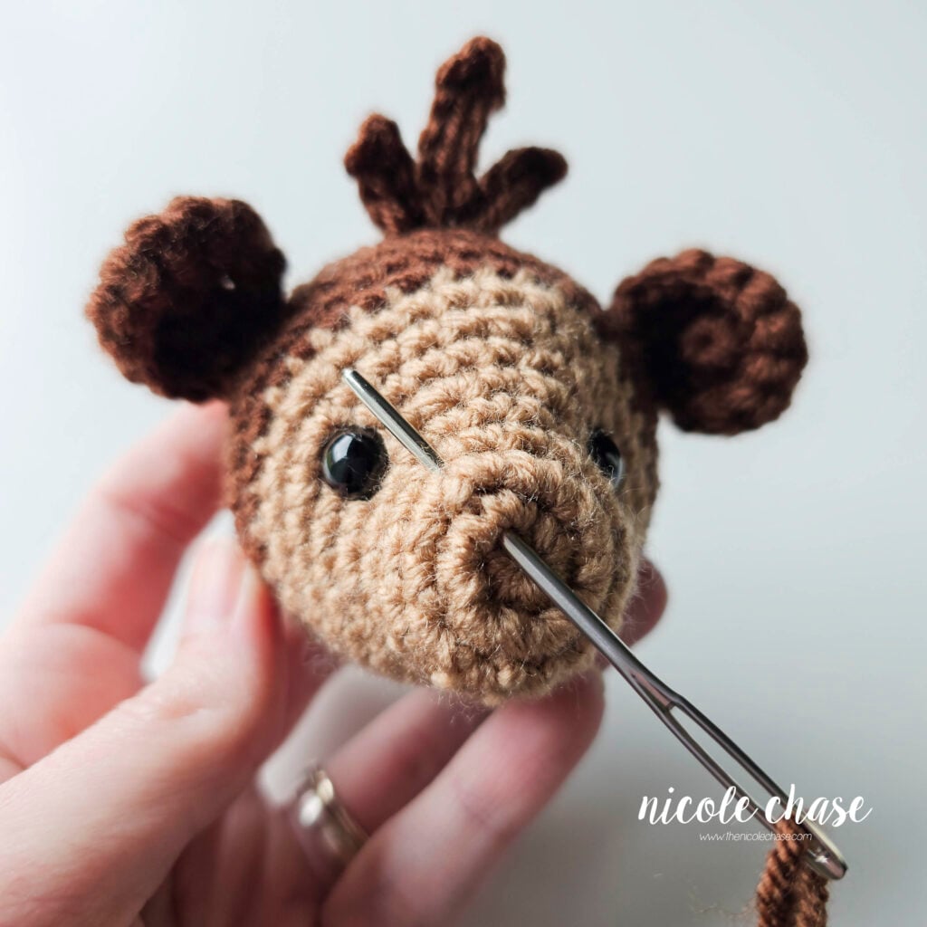 Embroidering the first nostril on the face of the crochet monkey with a yarn needle and dark brown yarn. 