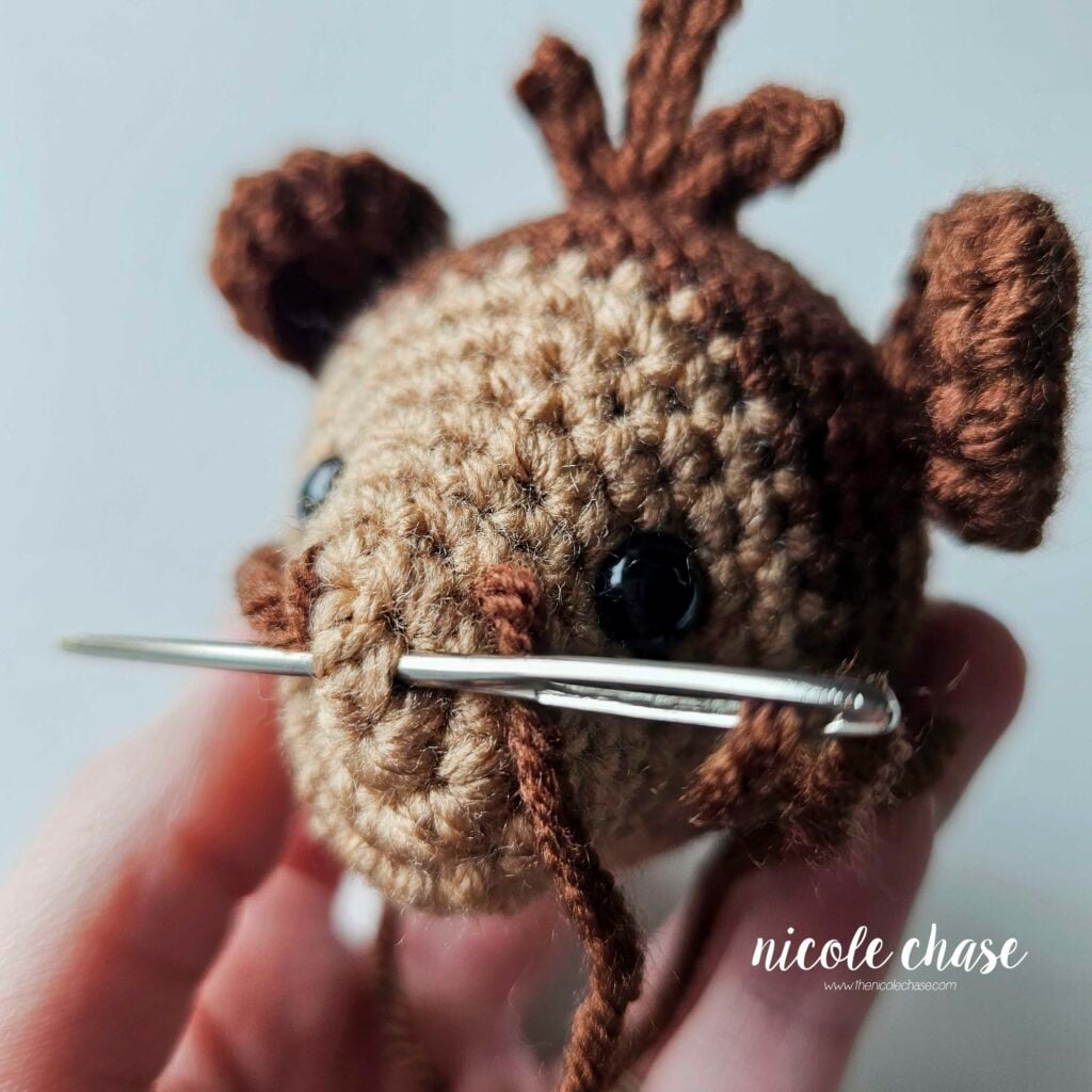 Finishing the second nostril on the crochet monkey's face and pushing the yarn needle through to bring the yarn tails together. 