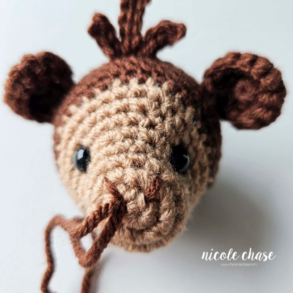 The nostrils have been embroidered on the front of the amigurumi monkey's face and the yarn tails are together for joining. 