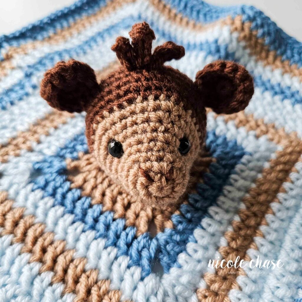 The amigurumi monkey head is placed in the middle of the striped square blanket and is awaiting assembly. 