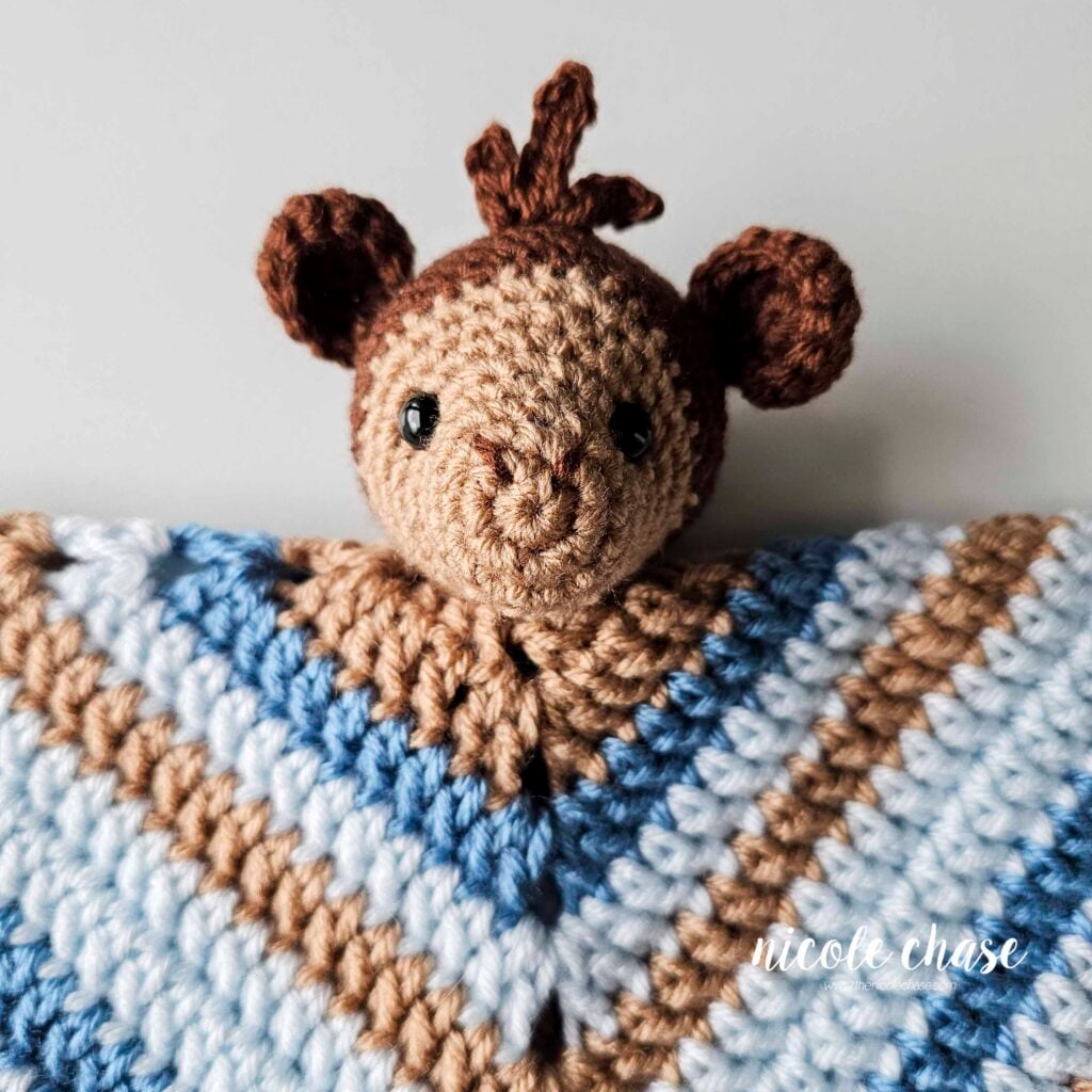 A view of the amigurumi monkey head sewn into place on the center of the blanket, with the blanket folded down. 