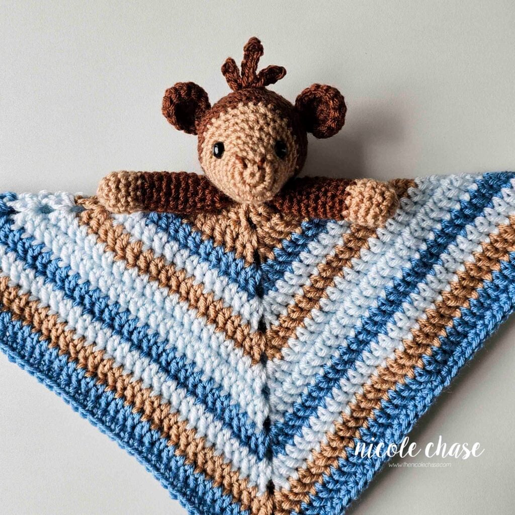 The monkey's crochet arms are sewn into place, and the blanket is folded down into a triangle shape, with the monkey head and arms sitting on top of the blanket. 