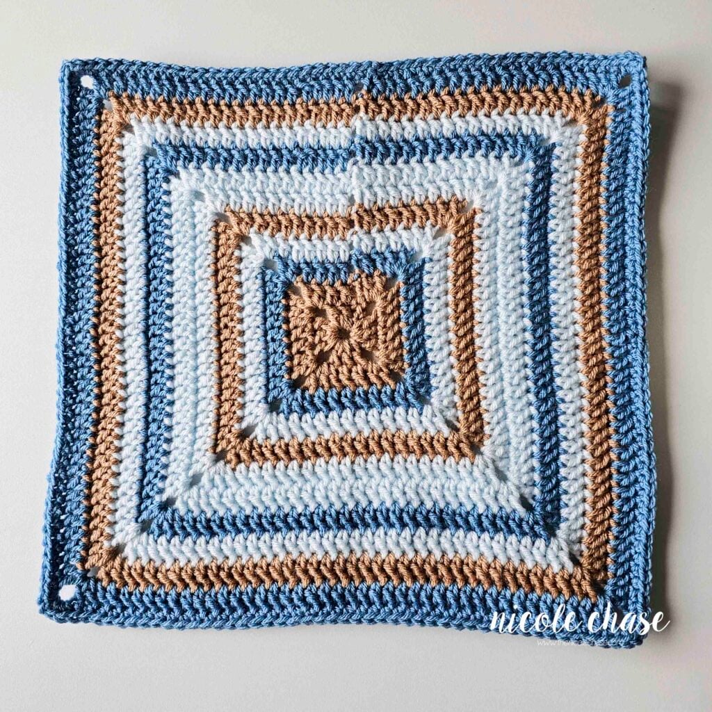 The finished blanket portion of the free monkey lovey crochet pattern shown in blue, light blue, and tan yarn, in stripes. The blanket is in the shape of a square and made in double crochet stitches.