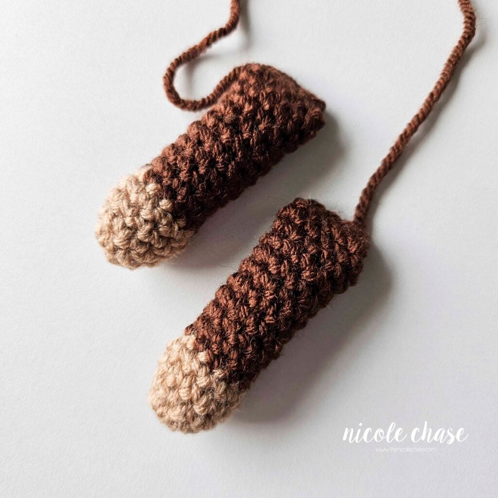 Two finished crochet arms made in dark brown yarn with light brown tips, filled with stuffing and awaiting assembly for this monkey lovey crochet pattern. 